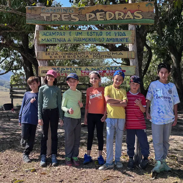 Grupo de crianças em frente à placa "Camping Três Pedras"